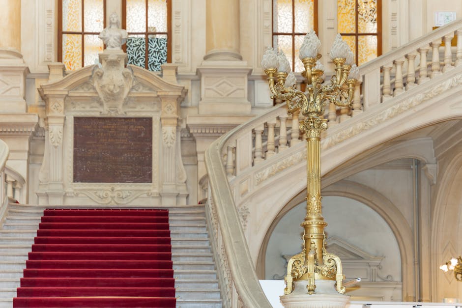 Elegant grand staircase with red carpet and ornate lamp post, showcasing classic architectural style.
