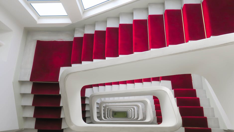 Elegant spiral staircase with vibrant red carpet, photographed from above in Lyon.